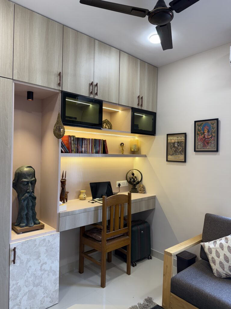 Modern study room featuring a light wood built-in desk with overhead storage lofts, backlit floating book shelving, integrated display niches showcasing sculptures and a wooden study chair.