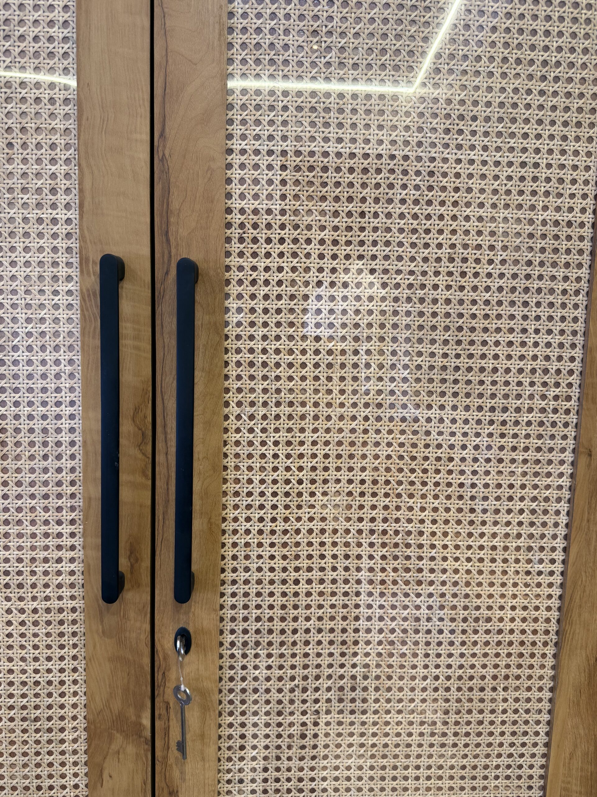 Close-up shot of a modern wooden wardrobe door featuring woven cane webbing panels, a sleek vertical black handle.