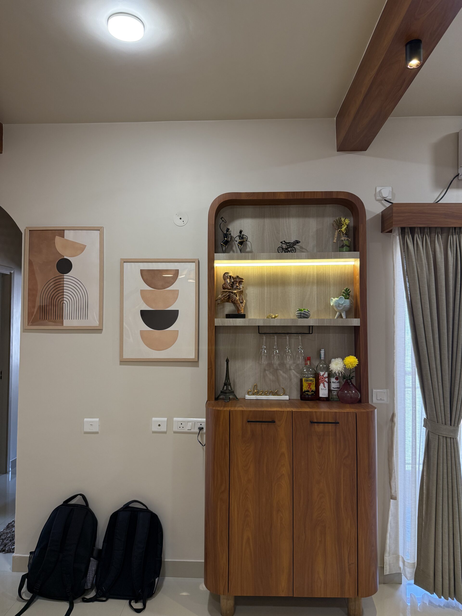 Custom-built wooden bar cabinet and display unit with a curved frame, integrated warm LED profile lighting, open shelves showcasing decor and glassware, and lower storage shutters.